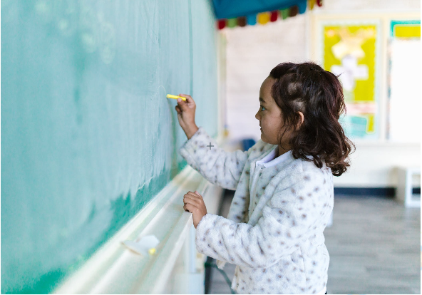 02 Child drawing on a light blue wall while standing near a ledge.